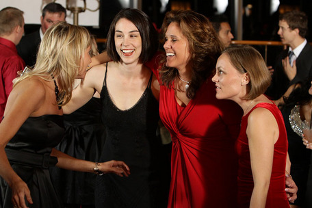 Gruppe elegant gekleideter Personen bei einer Veranstaltung, mit roten Kleidern und schwarzen Outfits vor belebtem Hintergrund.