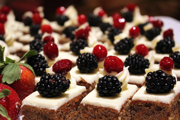 Nahaufnahme von Dessertwürfeln mit Kuchenboden, weißem Topping und Beeren, daneben Erdbeeren mit Grün.