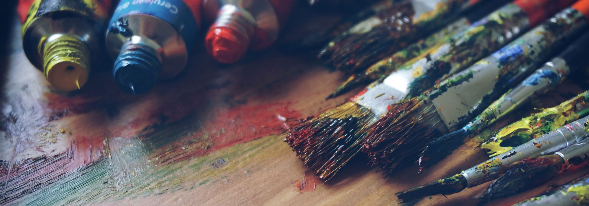 Farbkleckse auf Holzoberfläche mit Tuben und benutzten Pinseln.